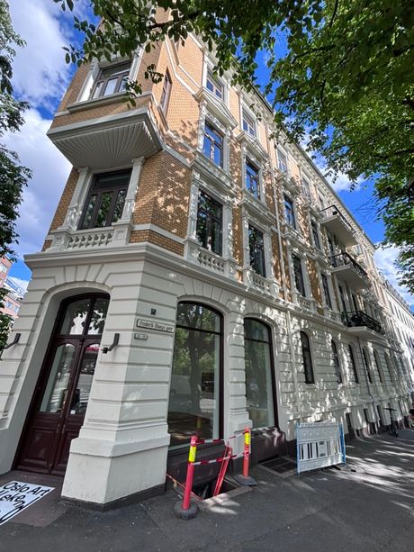 Hjørnet av en bygård med nymalt, lys fasade og avsperring på fortauet